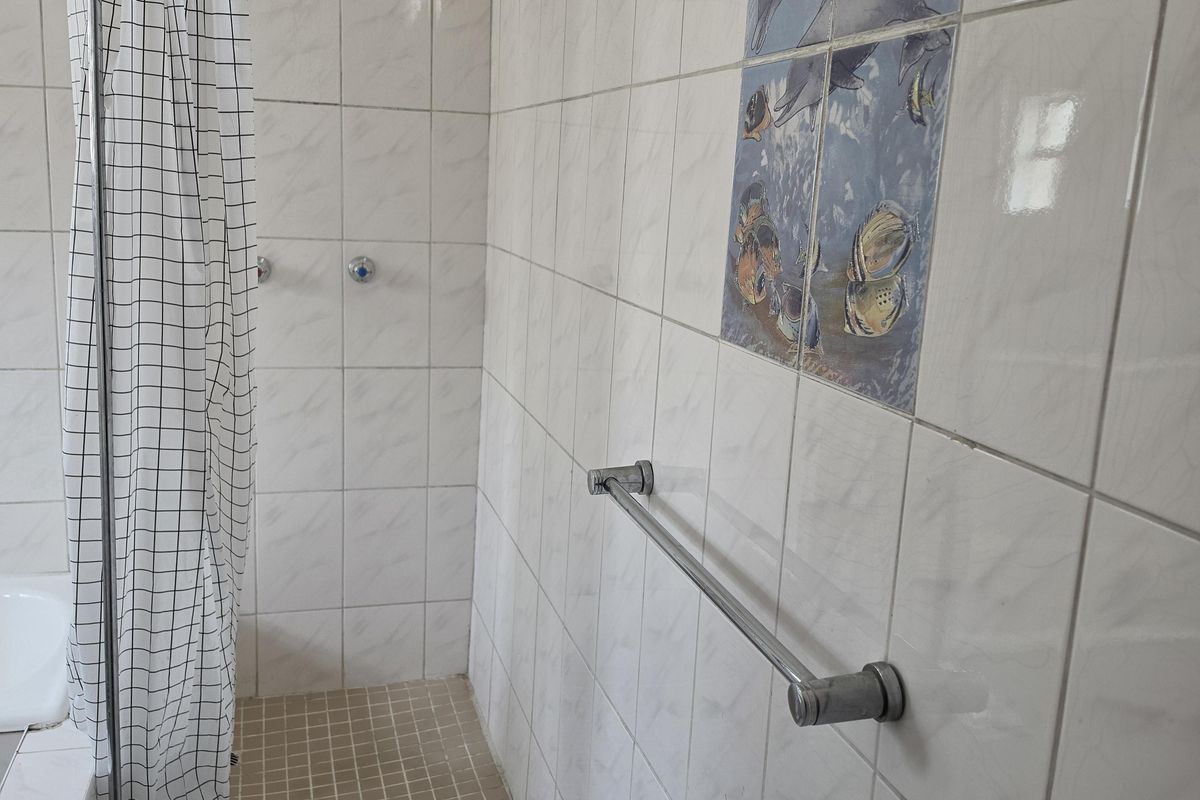 A functional bathroom shower area featuring white wall tiles, a built-in shower enclosure, and a chrome towel rail.