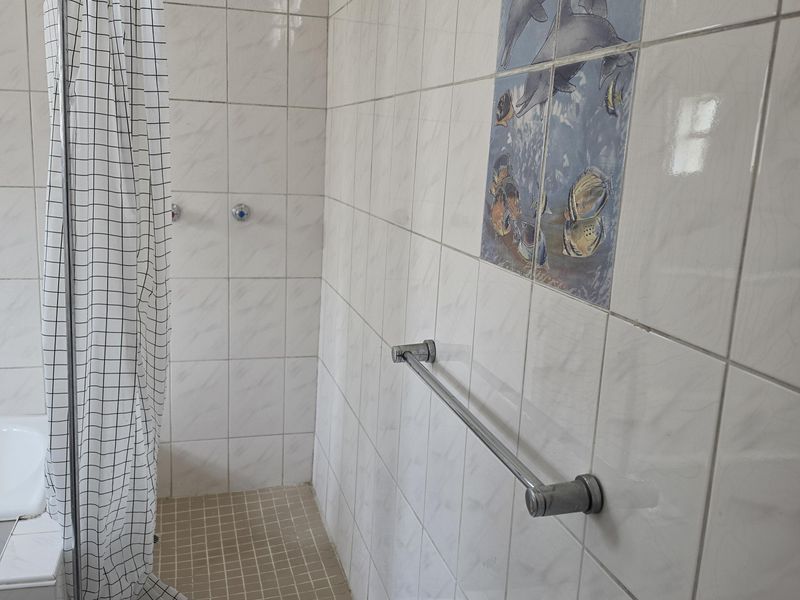 A functional bathroom shower area featuring white wall tiles, a built-in shower enclosure, and a chrome towel rail.
