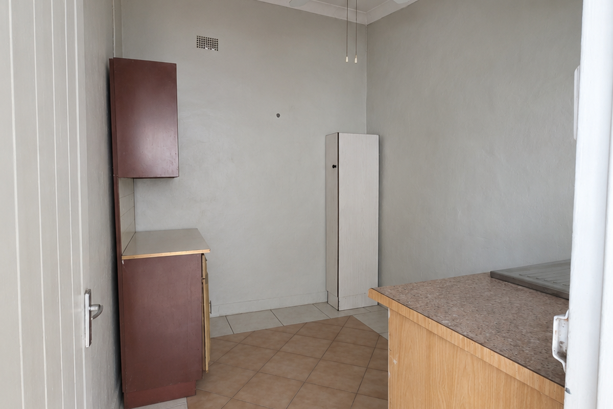 A functional scullery or utility area featuring built-in cabinetry, laminate countertops, tiled flooring, and a ceiling fan, offering potential for modernization.
