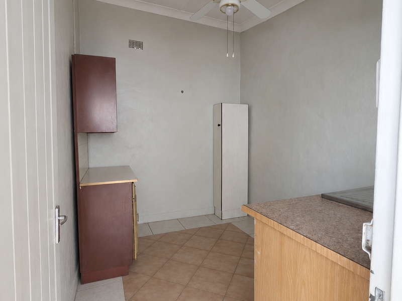 A functional scullery or utility area featuring built-in cabinetry, laminate countertops, tiled flooring, and a ceiling fan, offering potential for modernization.