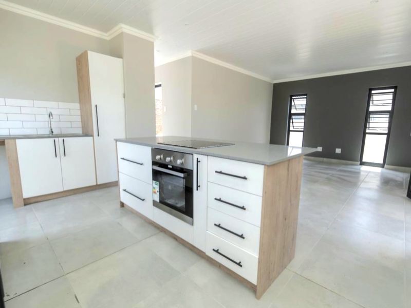 Modern open-plan kitchen featuring a central island with built-in oven and hob, sleek cabinetry, and neutral tiled flooring throughout the living space.