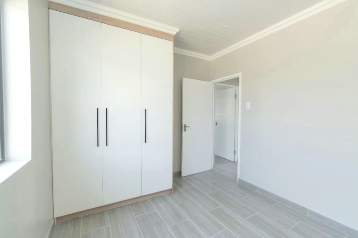 A bright, modern bedroom featuring neutral tiled flooring, a tongue and groove ceiling, and sleek built-in cupboards.