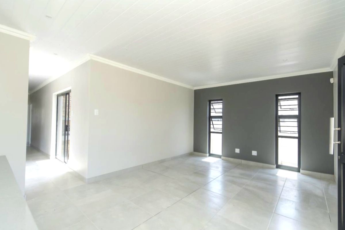 A bright, empty living area featuring neutral tiled flooring, a tongue and groove ceiling, and modern dark-framed windows.
