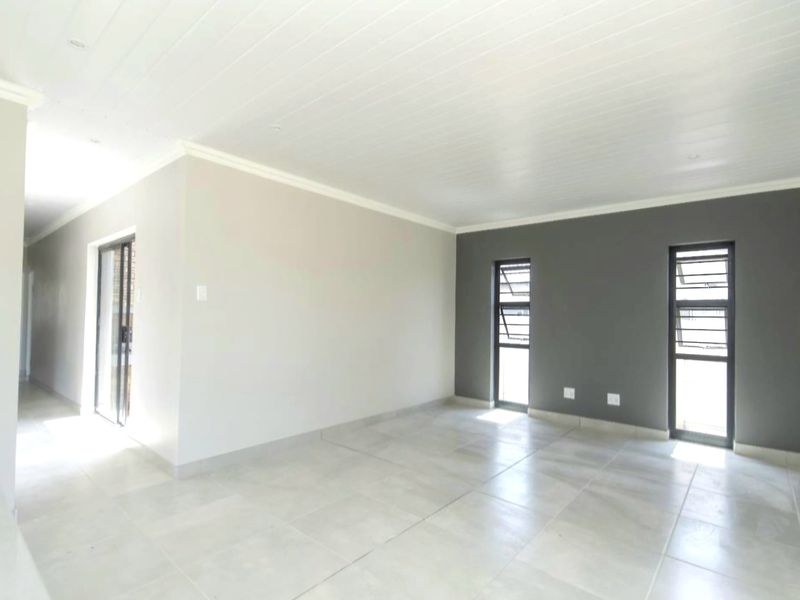 A bright, empty living area featuring neutral tiled flooring, a tongue and groove ceiling, and modern dark-framed windows.