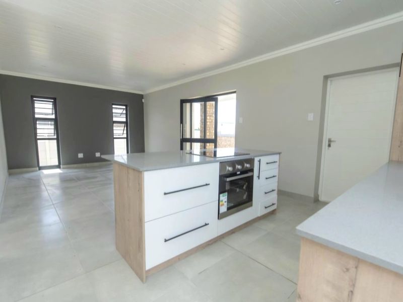 Modern open-plan living and kitchen area featuring a central island with built-in oven, stone countertops, and neutral tiled flooring throughout.