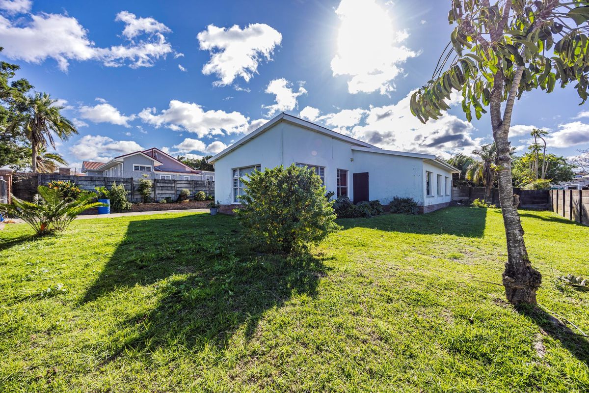 Rear view of the property featuring a spacious lawn and concrete boundary walls under a bright sky.