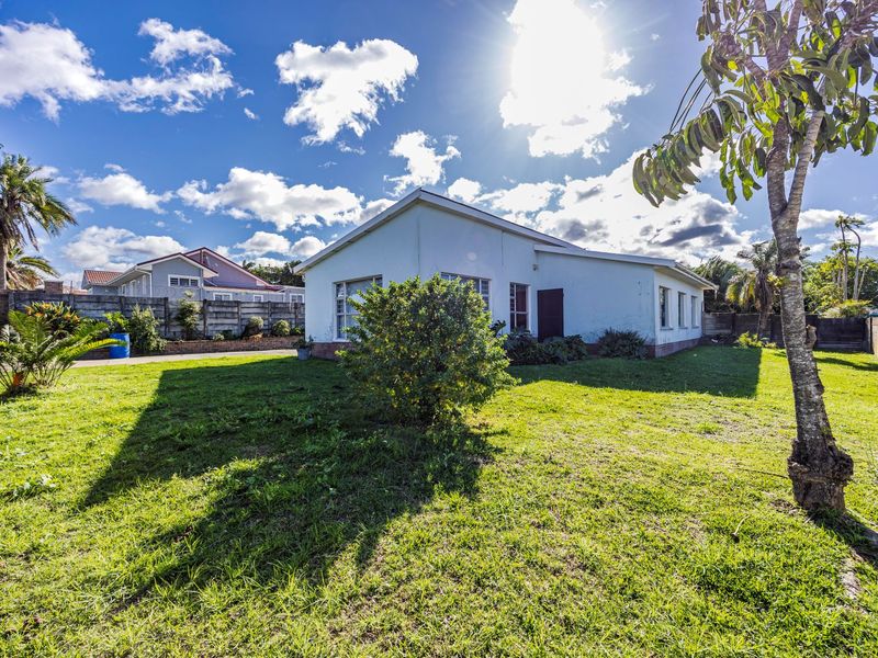 Rear view of the property featuring a spacious lawn and concrete boundary walls under a bright sky.