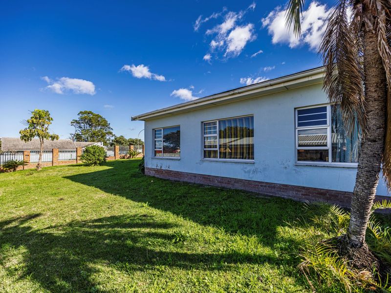 Rear view of the property showing the garden, brick perimeter wall, and exterior wall with aluminium window frames.