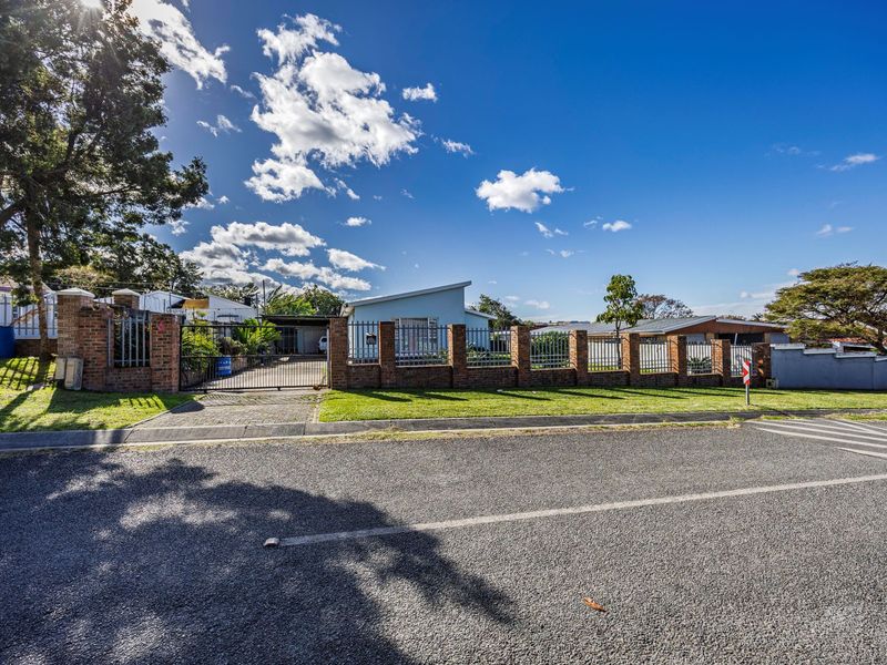 Front exterior view of the property featuring a brick boundary wall, metal security fencing, and a paved driveway leading to the house.