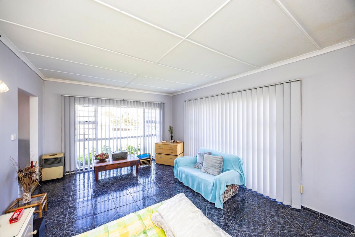 A living room featuring dark tiled flooring, large windows with vertical blinds, and a suspended ceiling, offering a functional space with potential for modernization.