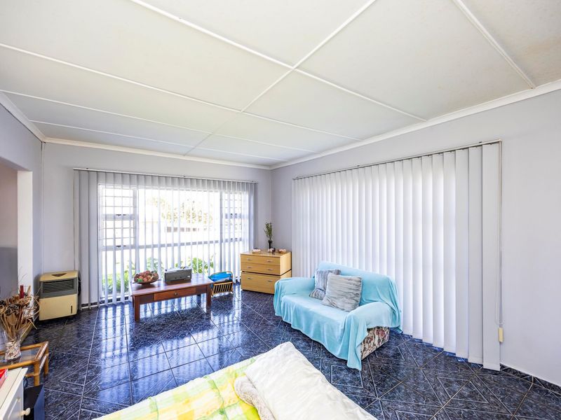 A living room featuring dark tiled flooring, large windows with vertical blinds, and a suspended ceiling, offering a functional space with potential for modernization.