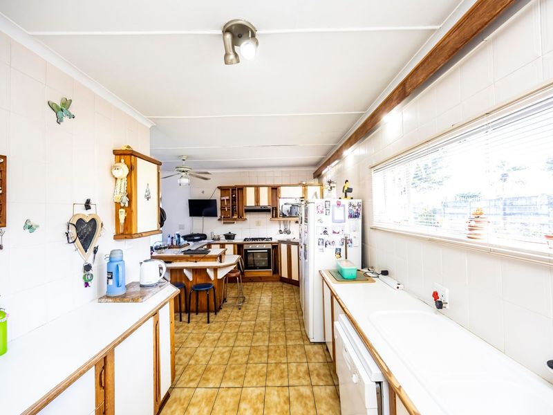 A functional kitchen featuring tiled flooring, wall-to-wall cabinetry, built-in oven and hob, and a double sink with ample counter space.