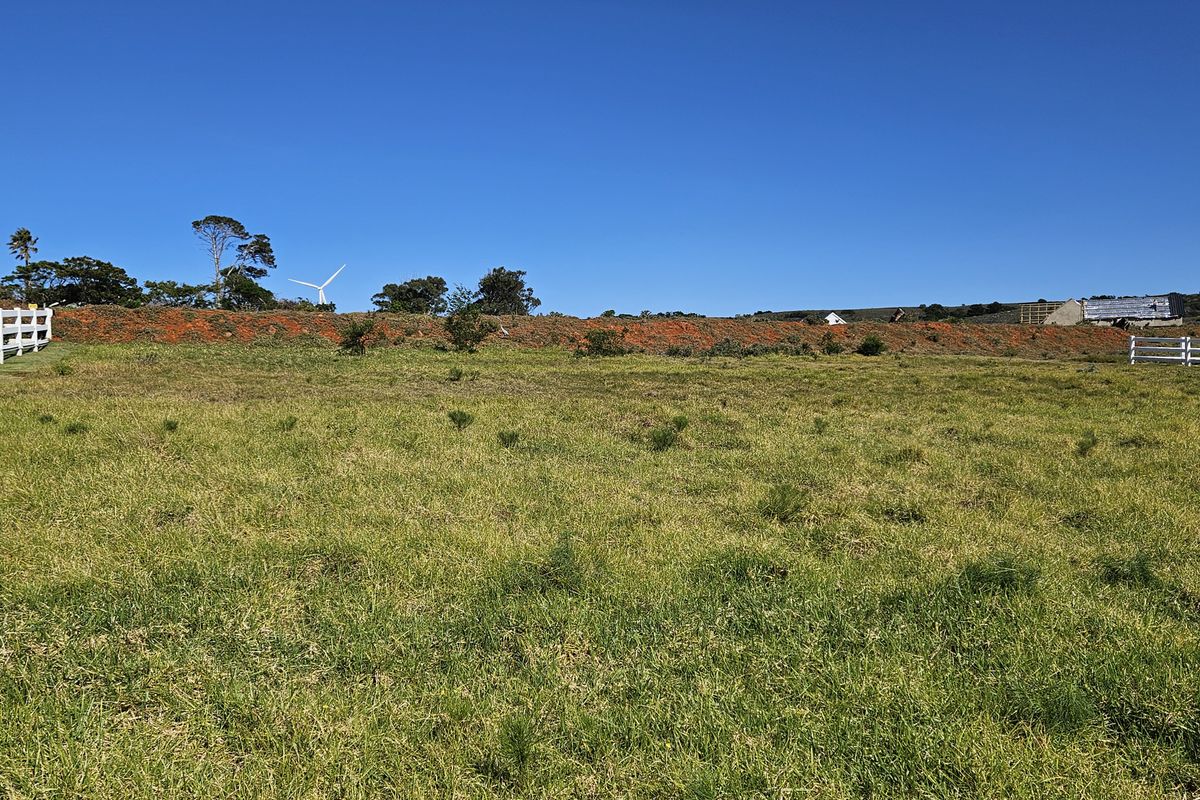 A view of the vacant residential land featuring open grassland and perimeter fencing under a clear blue sky.