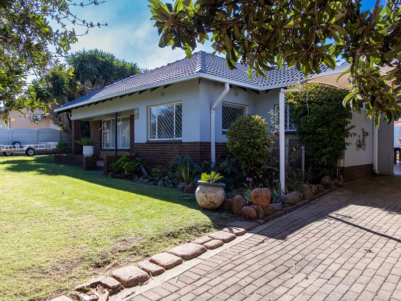 A well-maintained single-story house featuring a brick and plaster facade, tiled roof, paved driveway, and a neat front garden.