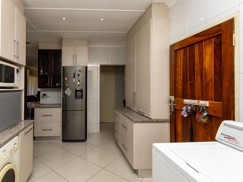 A functional scullery area featuring ample built-in cabinetry, granite countertops, tiled flooring, and integrated appliance space.