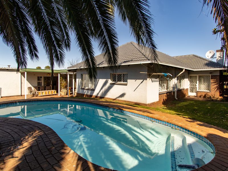 Rear view of the house featuring a swimming pool with brick coping, a covered patio area, and a tiled roof.