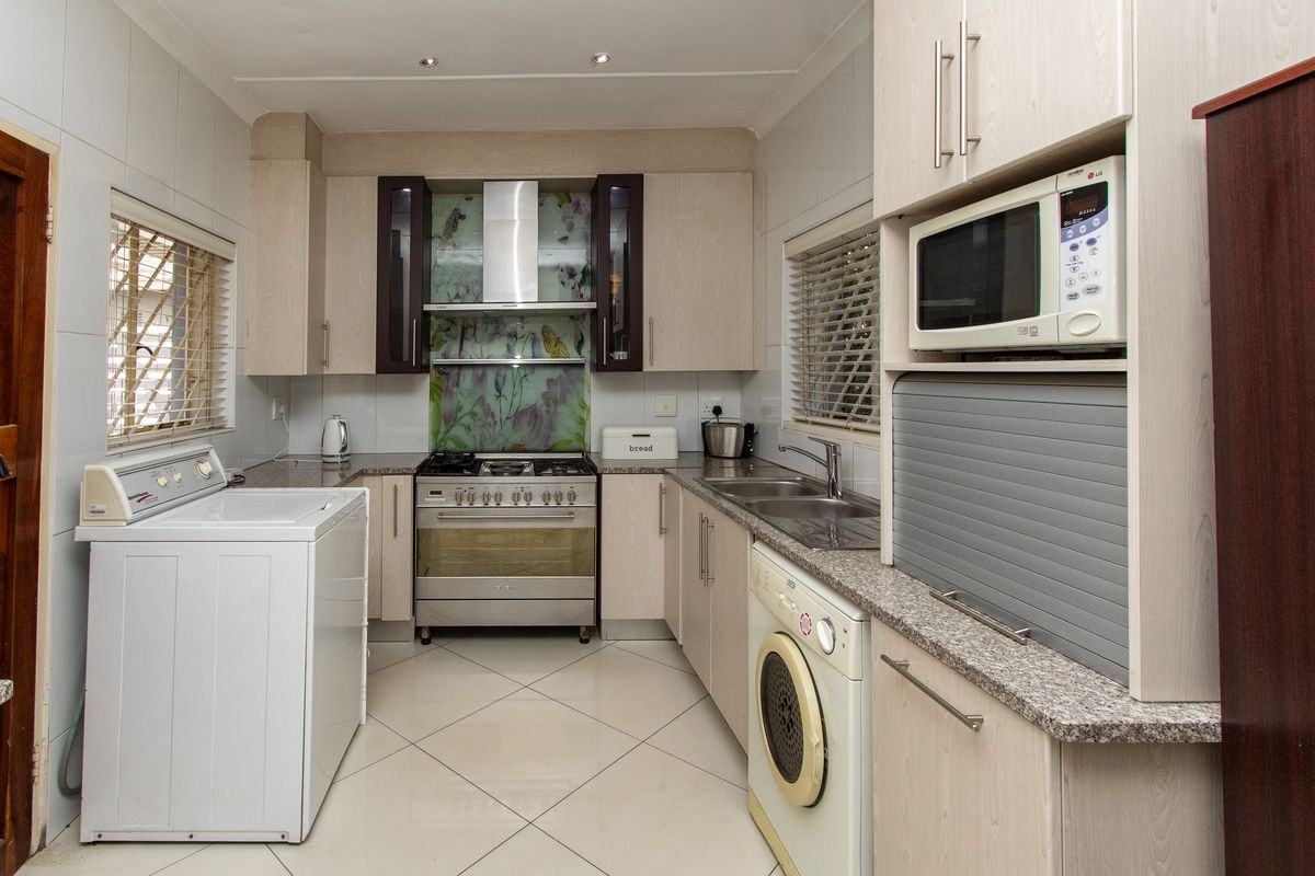 Functional kitchen featuring light wood cabinetry, granite countertops, a gas stove with extractor fan, and integrated laundry appliance connections.