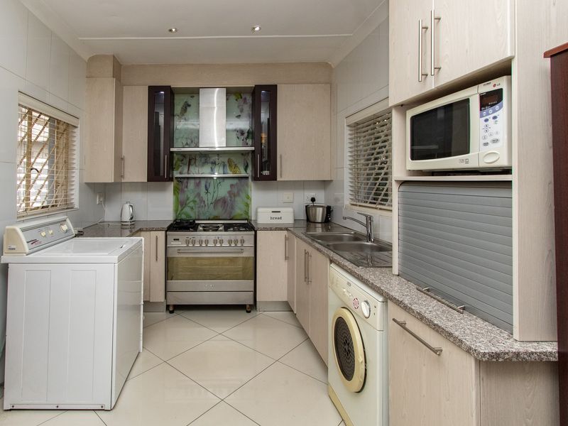 Functional kitchen featuring light wood cabinetry, granite countertops, a gas stove with extractor fan, and integrated laundry appliance connections.