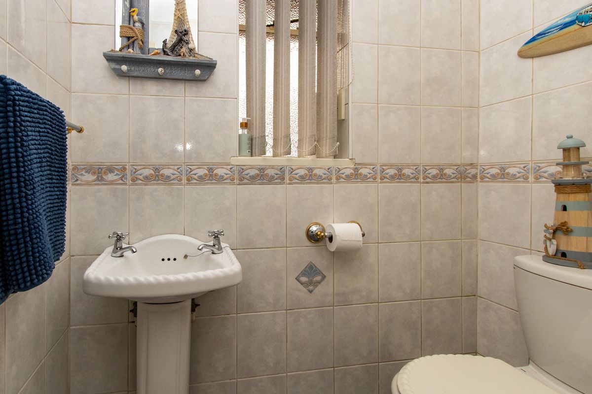 A compact bathroom featuring a pedestal basin, toilet, and neutral ceramic wall tiling with decorative border accents.