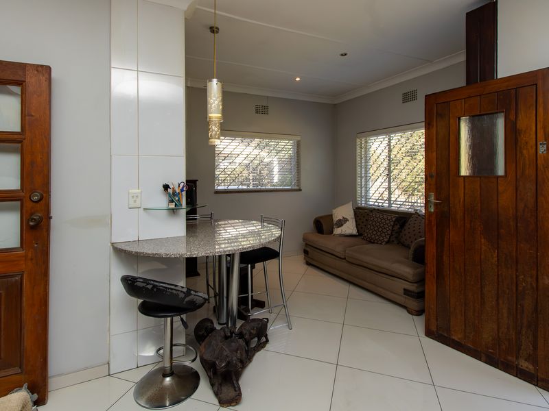Open plan living area featuring tiled flooring, a built-in granite breakfast bar, and timber doors, offering a functional and versatile space.