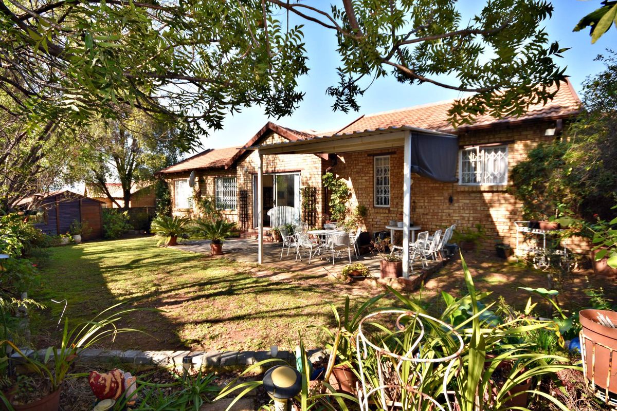 Rear view of the townhouse featuring a brick facade, a covered patio area, and a well-established garden.