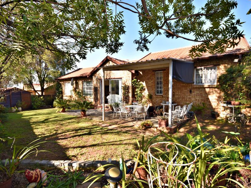 Rear view of the townhouse featuring a brick facade, a covered patio area, and a well-established garden.