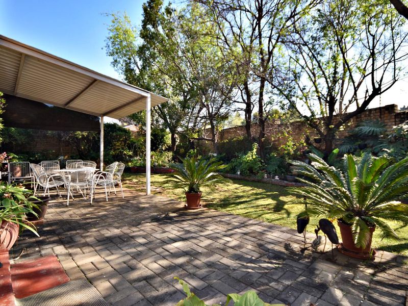 A covered outdoor patio area featuring paved flooring, overlooking a private garden with mature trees and a brick boundary wall.