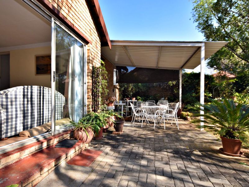 A covered paved patio area featuring a brick facade and sliding glass doors, providing a seamless transition to the garden space.