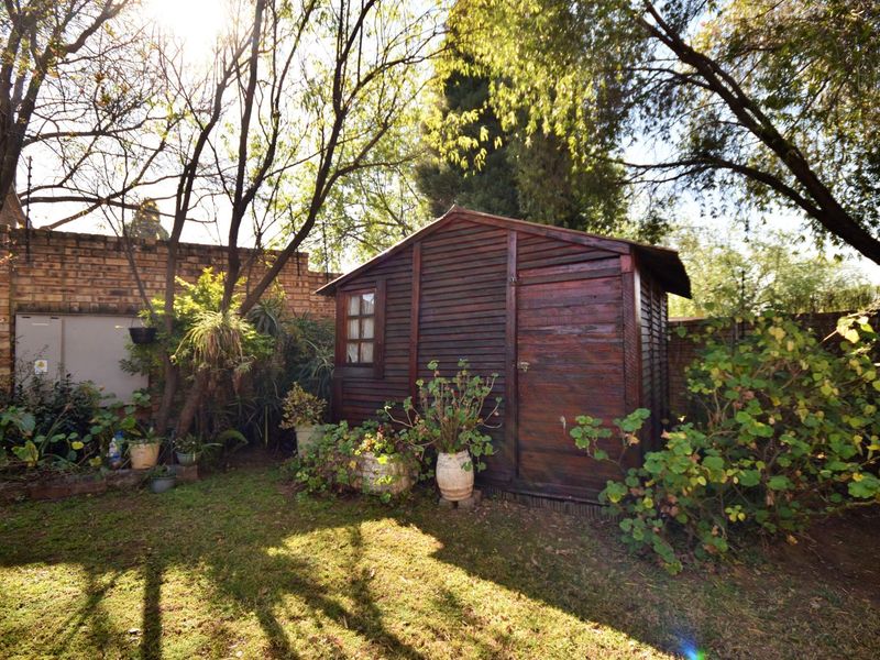 A private garden area featuring a wooden storage shed, established trees, and brick boundary walls.