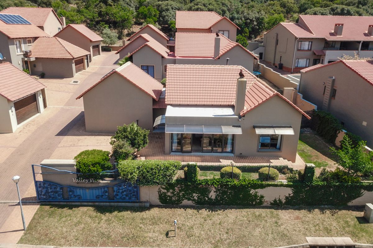 Aerial view of a residential property featuring a tiled roof, paved driveway, and a patio area within a suburban estate setting.
