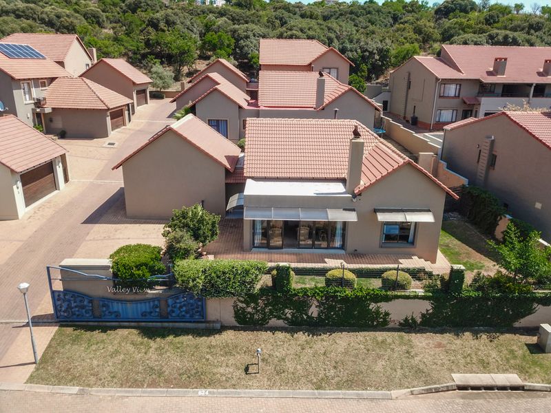 Aerial view of a residential property featuring a tiled roof, paved driveway, and a patio area within a suburban estate setting.