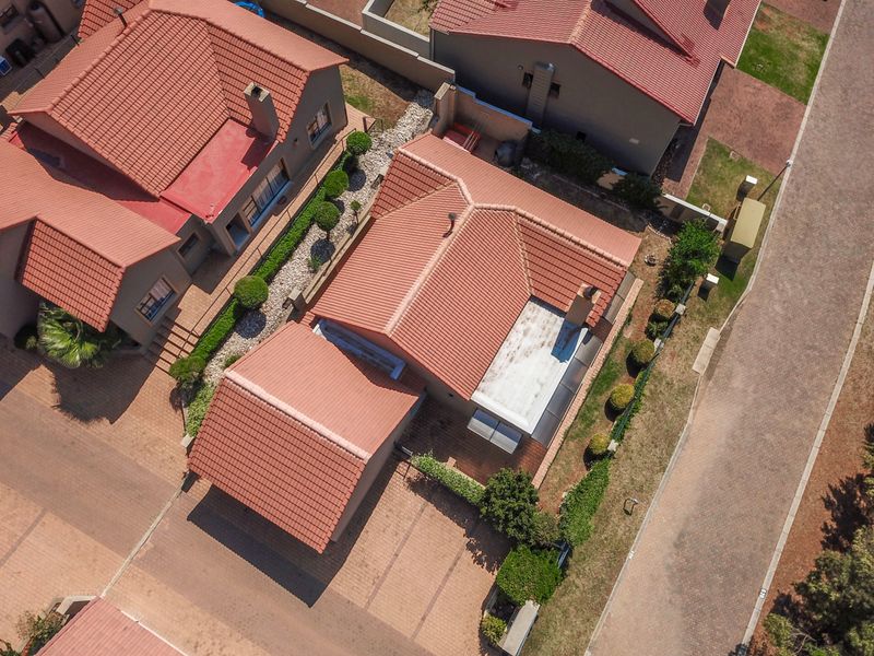Aerial view of a residential property featuring a tiled roof, paved driveway, and surrounding boundary walls within a suburban estate setting.