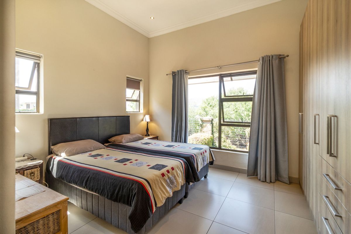 A well-maintained bedroom featuring neutral tiled flooring, built-in cupboards, and large windows that provide ample natural light and garden views.