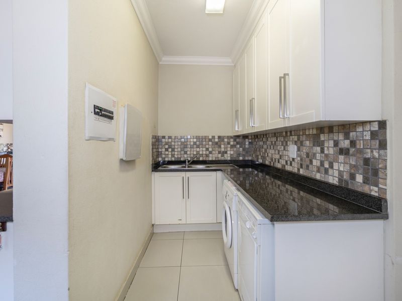 A functional laundry area featuring white built-in cabinetry, dark granite countertops, a mosaic tile backsplash, and a stainless steel sink.