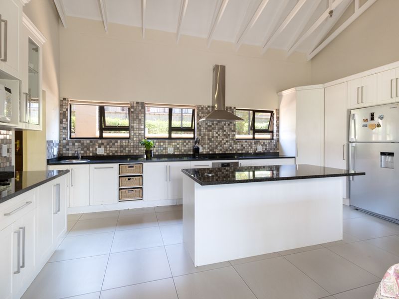 Spacious kitchen featuring white cabinetry, granite countertops, a central island, and a vaulted ceiling with exposed beams, creating an open and airy atmosphere.