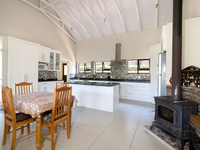 Spacious open-plan kitchen and dining area featuring a vaulted ceiling with exposed rafters, a central island, and a prominent wood-burning fireplace.