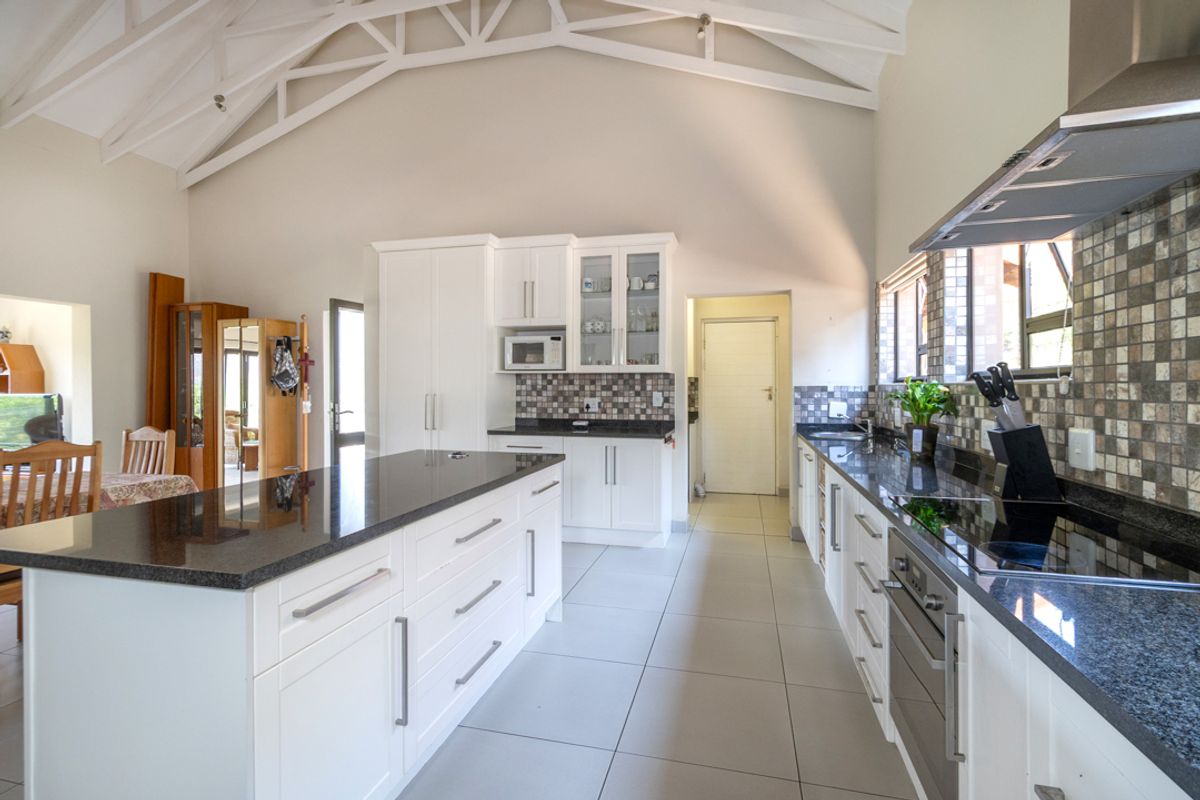 Spacious kitchen featuring a large island, granite countertops, built-in appliances, and a high vaulted ceiling with exposed white trusses.
