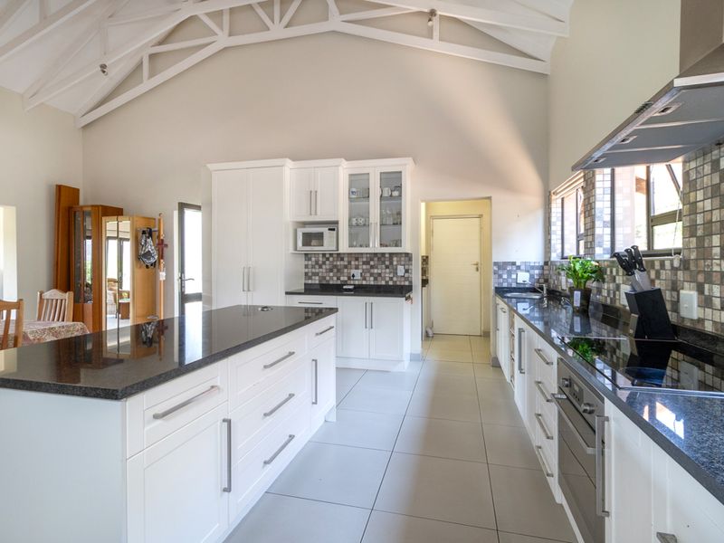 Spacious kitchen featuring a large island, granite countertops, built-in appliances, and a high vaulted ceiling with exposed white trusses.