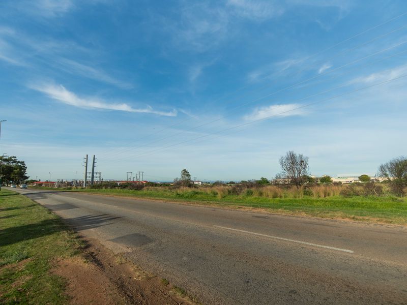A view of the asphalt road and surrounding vacant land with visible utility infrastructure and power lines.