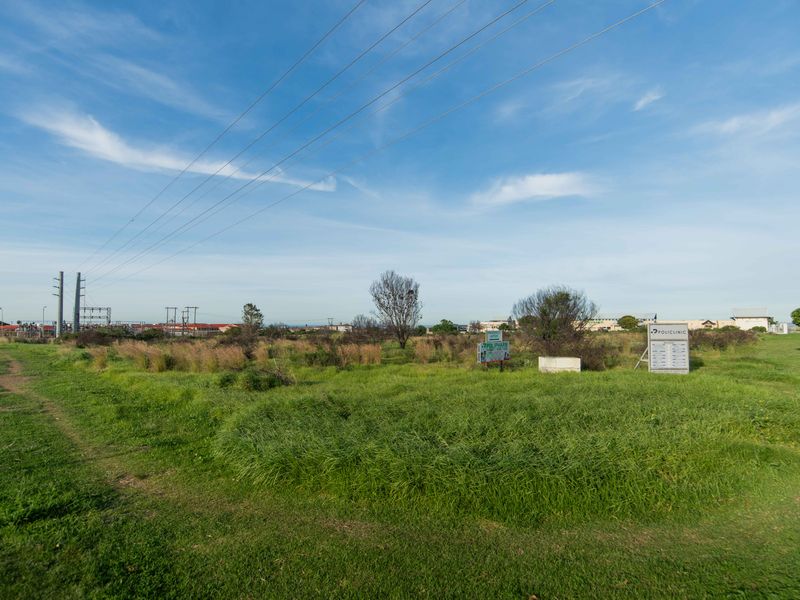 A vacant residential plot featuring natural grass coverage, overhead power lines, and existing signage on the property.
