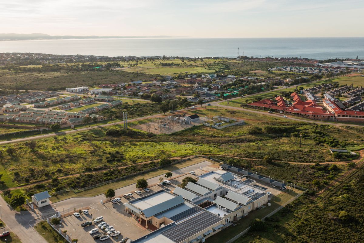 Aerial view of a commercial property complex featuring solar panels, paved parking, and surrounding residential development with coastal views.