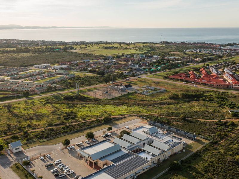 Aerial view of a commercial property complex featuring solar panels, paved parking, and surrounding residential development with coastal views.