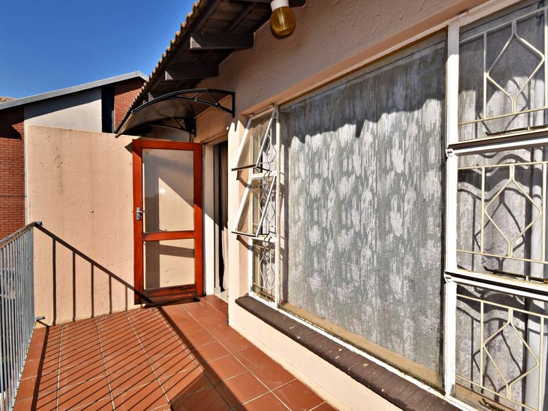 A balcony area featuring tiled flooring, a metal balustrade, and security-fitted windows and door, providing an outdoor space for the apartment.