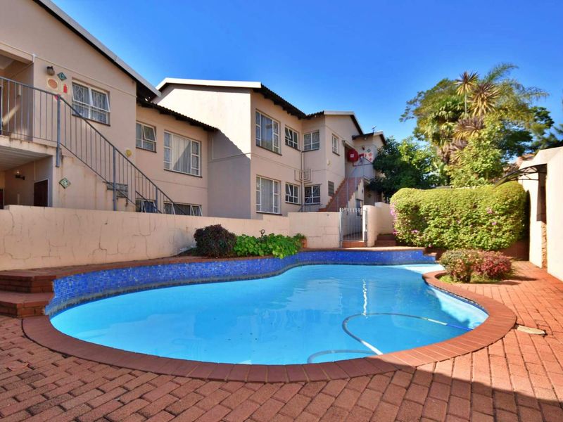 Communal swimming pool area featuring brick paving, a boundary wall, and access to the apartment building via external metal staircases.