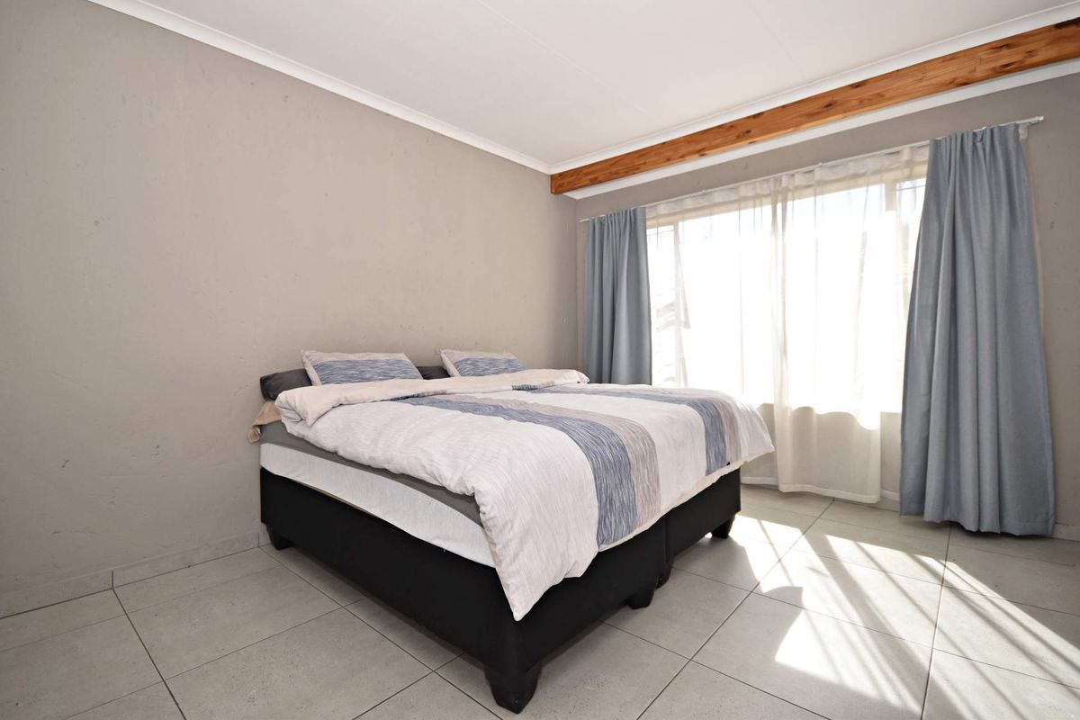 A bedroom featuring tiled flooring, an exposed timber ceiling beam, and large windows with curtain tracks allowing for natural light.