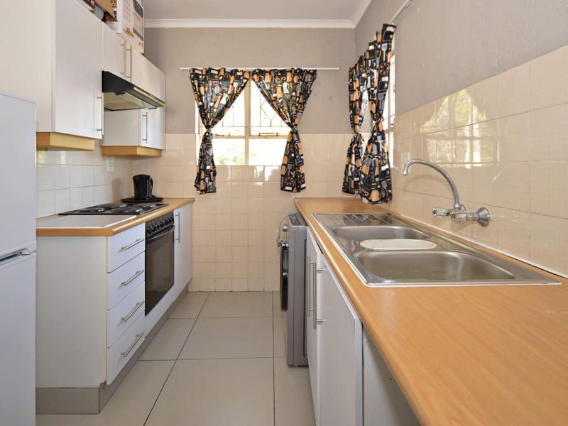A functional galley-style kitchen featuring laminate countertops, built-in cabinetry, an electric hob, oven, and a stainless steel double sink with tiled splashbacks.