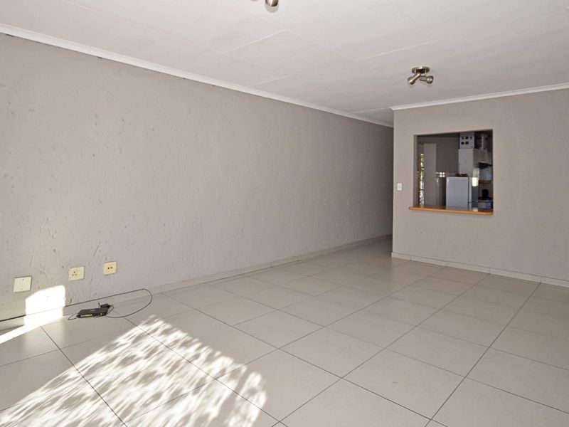 An empty, neutrally painted living area featuring tiled flooring and a convenient serving hatch connecting to the kitchen space.
