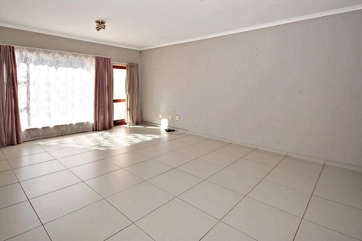 A spacious, empty living room featuring neutral tiled flooring, a large sliding glass door for natural light, and plain wall finishes.