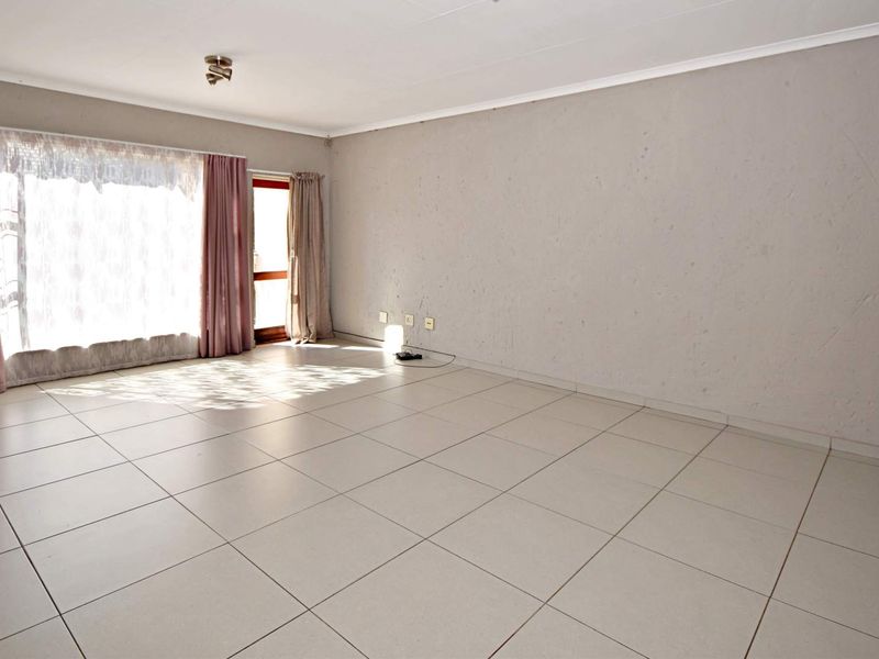 A spacious, empty living room featuring neutral tiled flooring, a large sliding glass door for natural light, and plain wall finishes.