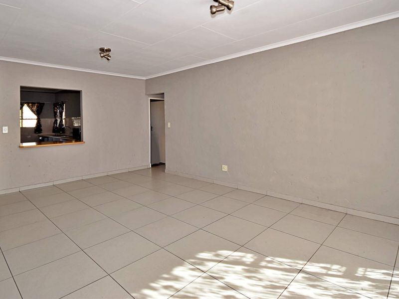 A spacious, empty living area featuring neutral tiled flooring, coved ceilings, and a convenient pass-through window connecting to the kitchen space.